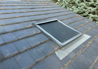 Fenêtre de toit de marque VELUX® posée avec son capot de protection fermé intégration parfaite dans la couverture en tuiles plates foncées avec solin périphérique pour l’étanchéité