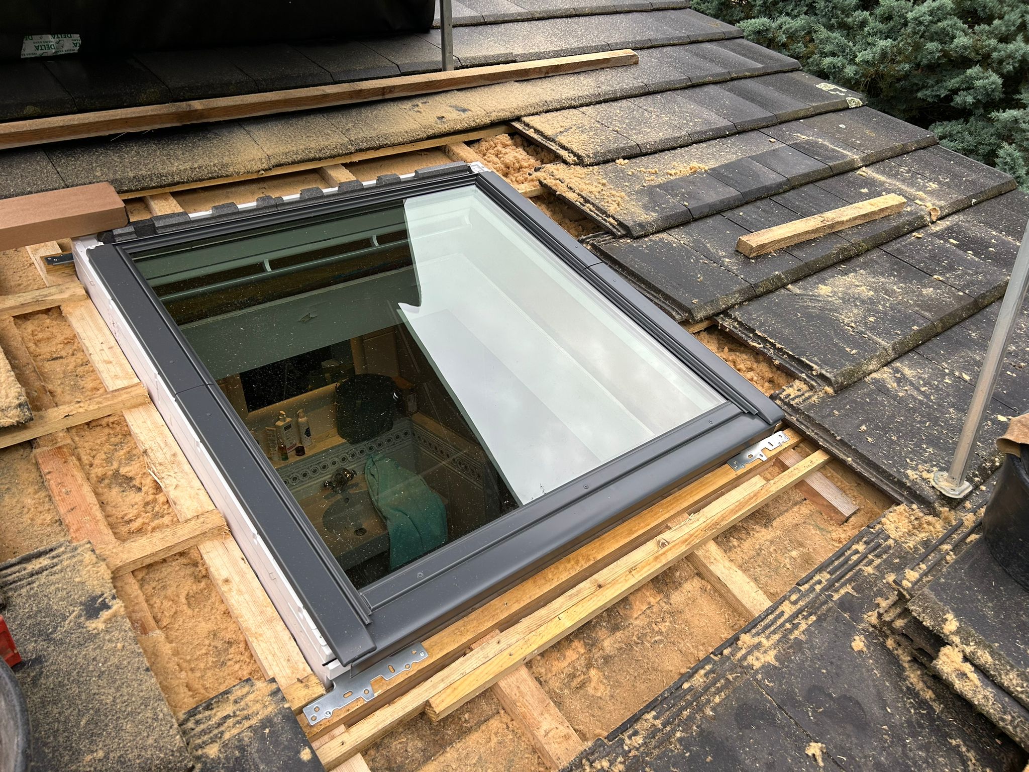 Fenêtre de toit VELUX® posée vue depuis l’extérieur pendant les travaux avant repose complète des tuiles on voit la charpente apparente et l’isolation périphérique